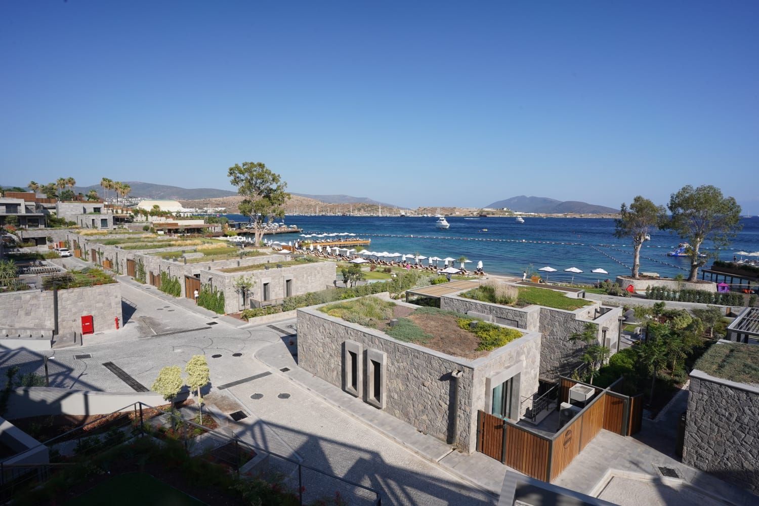 Yeşil çatılı taş villalar, arkada kumsal ve koy